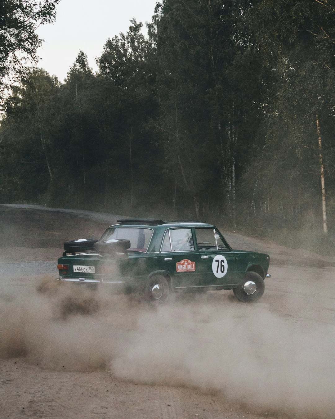 vintage green sedan with 76 number near passing trees