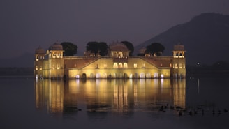 A grand view of Jagat Niwas Palace Hotel illuminated at dusk with the serene Lake Pichola in the foreground.