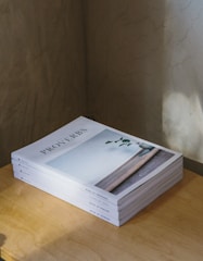A stack of books titled 'Proverbs' is neatly arranged on a wooden surface. The top book features an image of a vase with a single green branch against a serene background. Soft lighting casts subtle shadows on the surface.