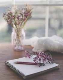 shallow focus photo of purple flowers on white spiral notebook