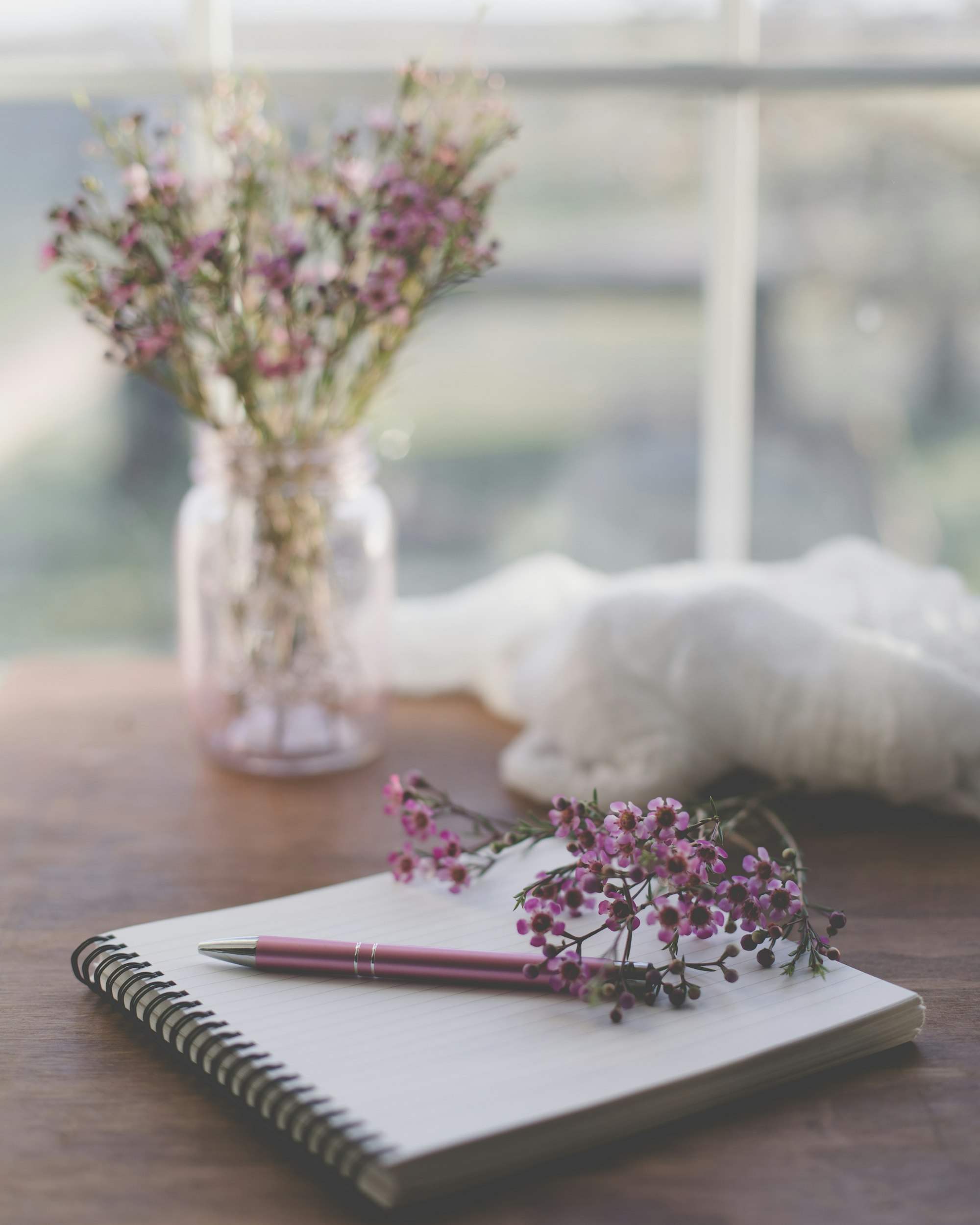 Writing desk with notebook, pen and pink flowers.