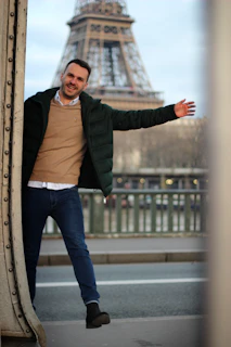 A happy young professional holding a suitcase, standing in front of a famous European landmark on a bright day.