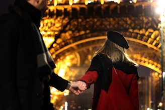A stylish couple walking hand in hand along the Seine river at night.