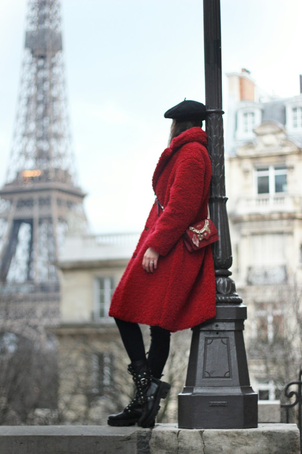 woman in red coat leaning on post lamp