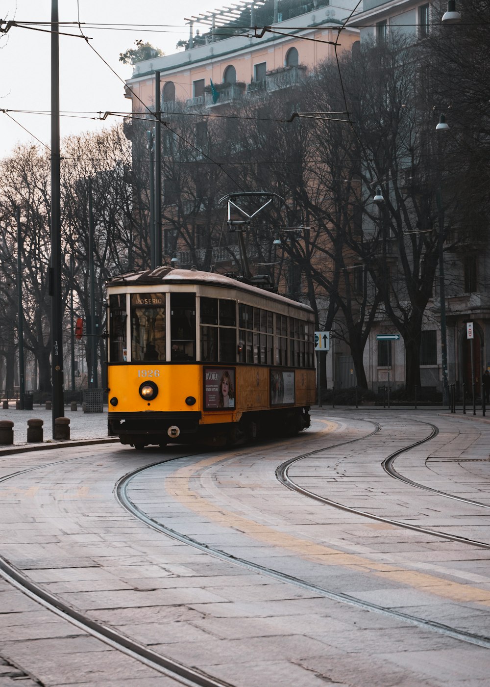 yellow tram crossing rail beside bare trees