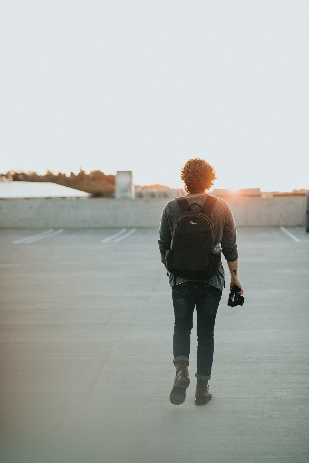 man wearing black backpack walking in front of the sun