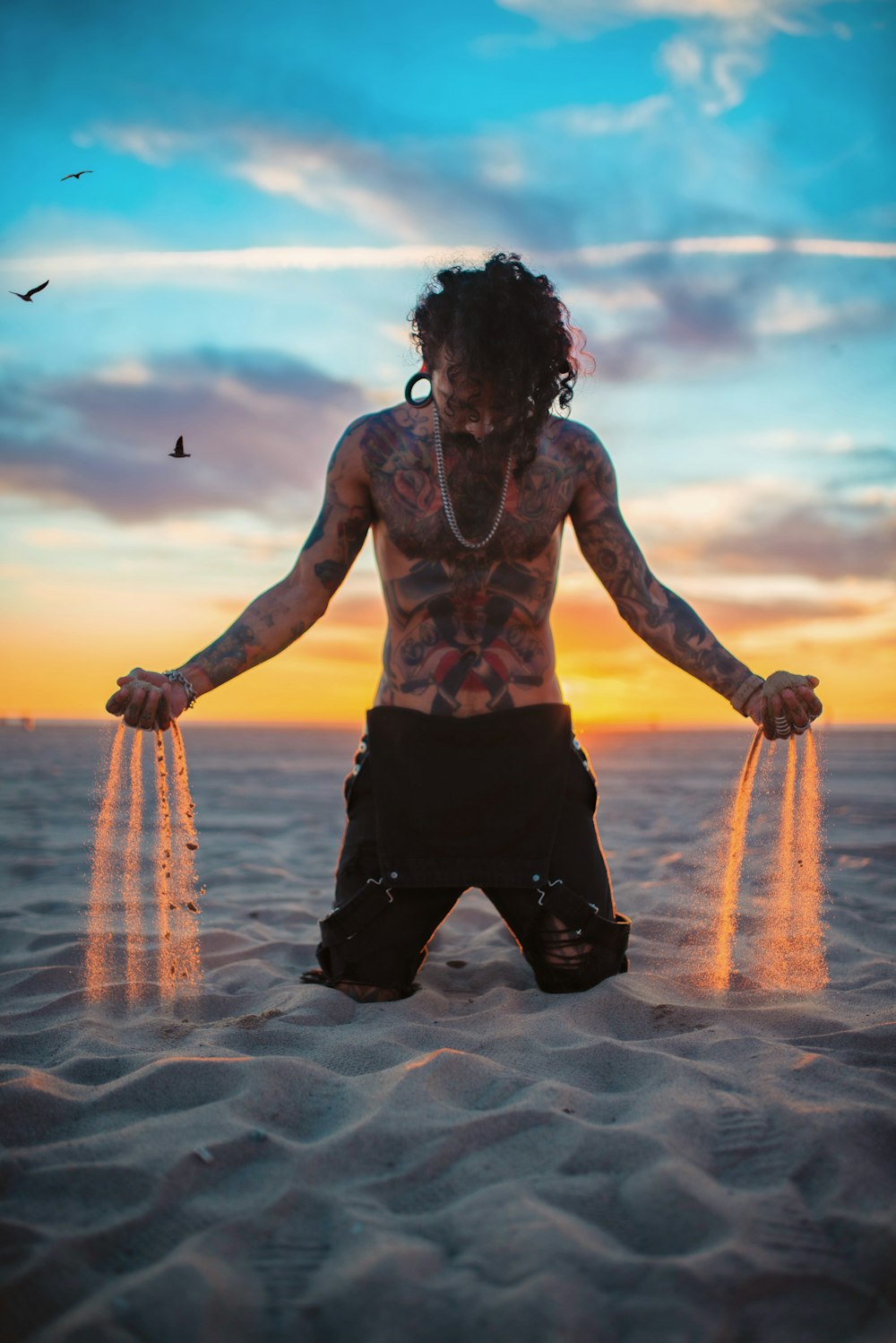 a man with tattoos standing in the sand