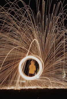Sparks fly in circular patterns creating a hypnotic visual effect, with a person standing in the middle wearing a yellow coat.
