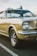 A classic beige Ford Mustang with chrome detailing and distinctively styled wheels. The image captures the car from a low angle, highlighting its retro features and iconic shape. The background shows a blurred outdoor setting, and the lighting suggests a late afternoon ambiance.