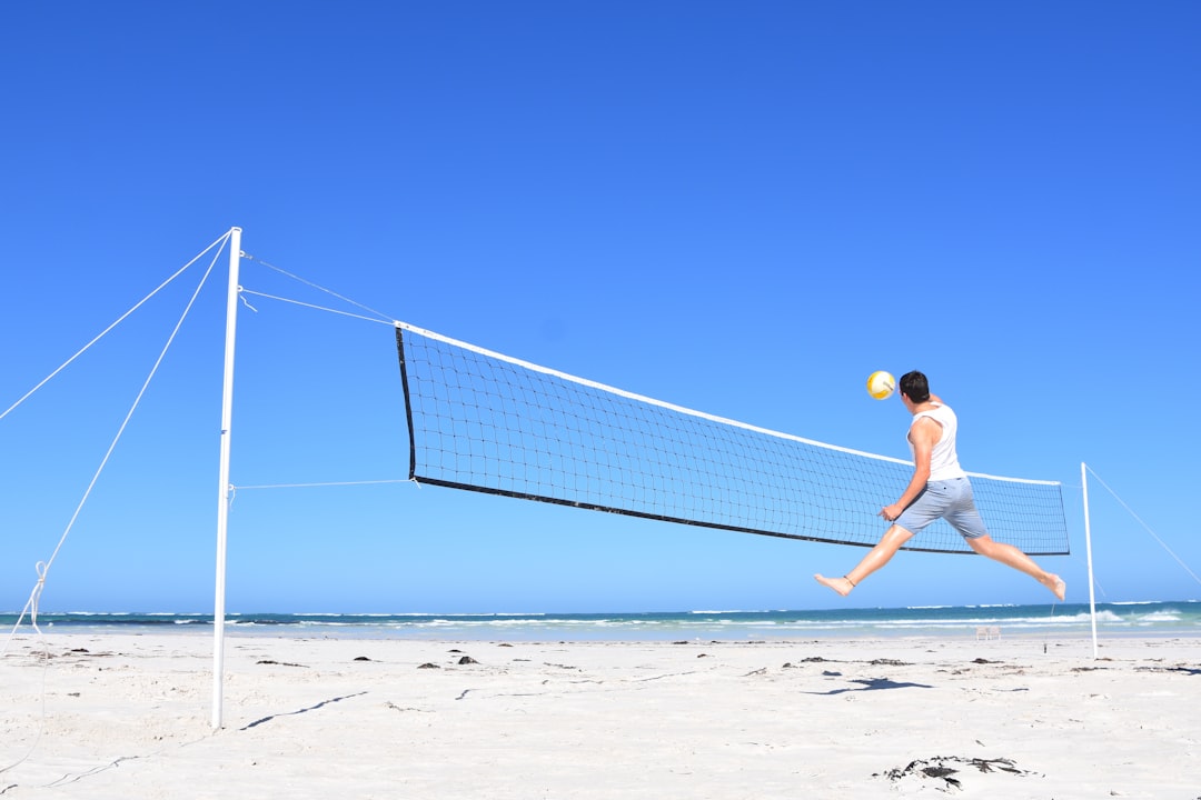 photography of man playing volleyball on sand during daytime