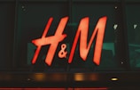 A bright, red neon sign with the letters 'H & M' displayed against a dark glass background.