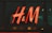 A bright, red neon sign with the letters 'H & M' displayed against a dark glass background.