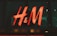 A bright, red neon sign with the letters 'H & M' displayed against a dark glass background.