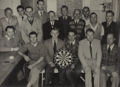 A warmly lit room with members of Finsbury Archers Lodge No. 5466 gathered around, sharing stories and camaraderie.