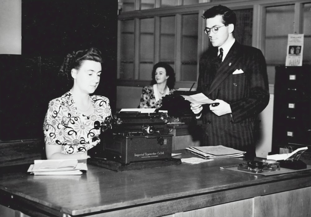 a man and a woman sitting at a desk with a typewriter