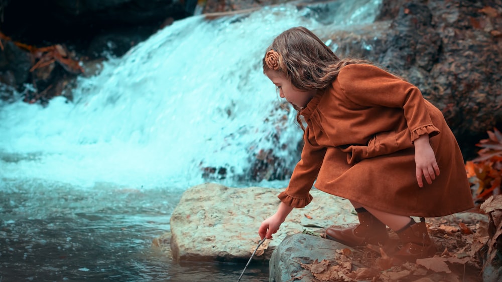 girl in brown long-sleeved dress beside body of water