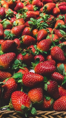A pile of fresh, ripe strawberries with vibrant red hues and green leafy tops, arranged in a close-up view. The strawberries fill the entire frame, showcasing their natural textures and seeds.