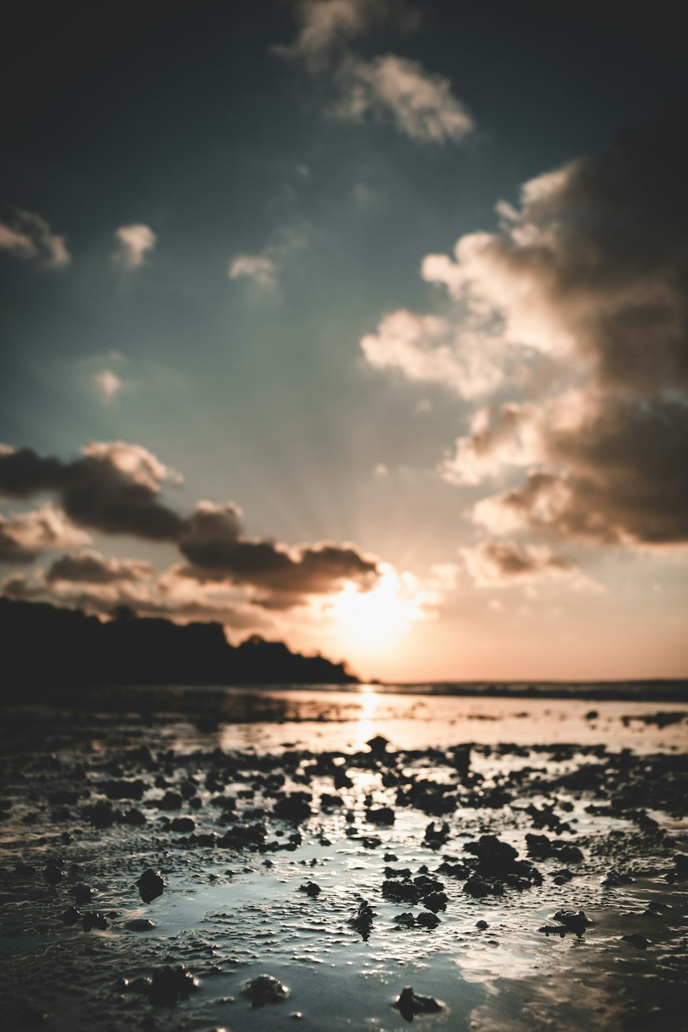 the sun is setting over the ocean with rocks in the water