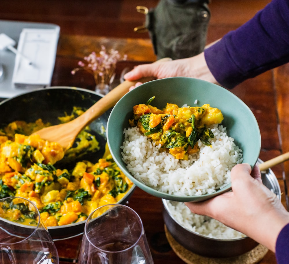 person holding spatula with vegetable and bowl with food