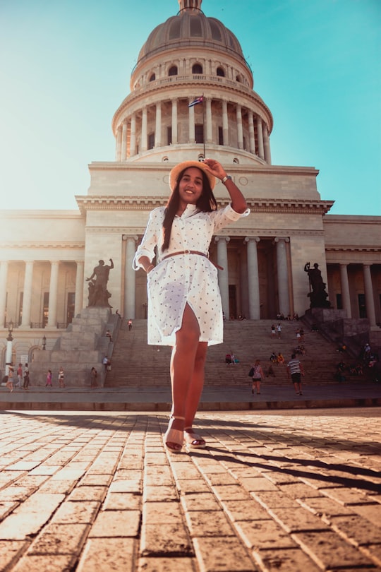 woman in white long-sleeved slit dress standing near structure in National Capital Building Cuba
