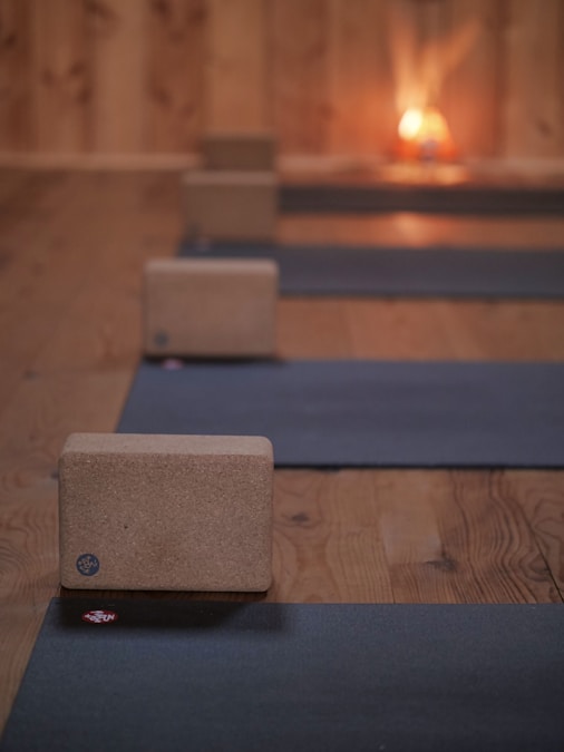 Row of dark yoga mats unrolled on a wooden floor with cork blocks beside them