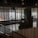 The image captures an indoor space with modern decor, featuring a large window that allows for a view of the distant cityscape. The space includes seating arrangements and some indoor plants, while vertical lines from the design elements add a sense of structure and division.