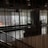 The image captures an indoor space with modern decor, featuring a large window that allows for a view of the distant cityscape. The space includes seating arrangements and some indoor plants, while vertical lines from the design elements add a sense of structure and division.