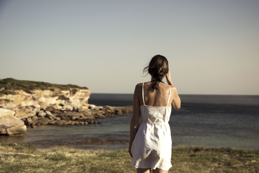 woman standing on grass field facing the sea