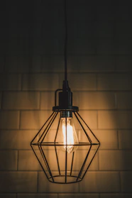 A warm industrial cage pendant light hanging over a rustic wooden table.