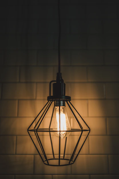 A sleek industrial cage pendant light glowing warmly over a rustic wooden table.