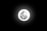 A bright full moon is centered against a dark night sky, displaying detailed craters and a glowing aura surrounding it.