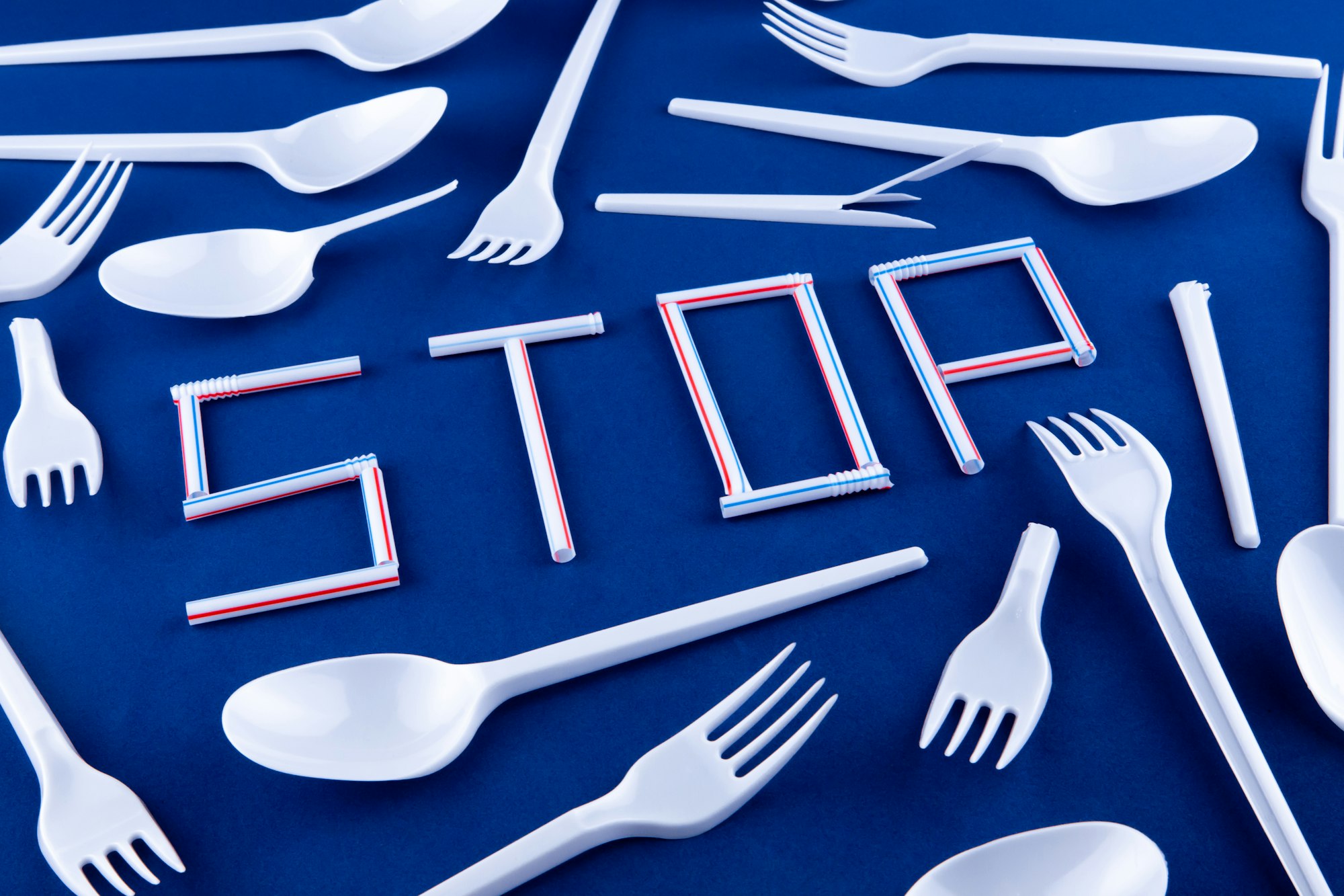 Plastic cutlery surrounding straws arranged to spell the word stop