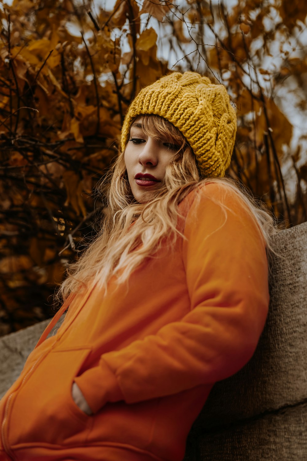 mulher na jaqueta laranja sentada no banco de madeira marrom