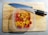 A plastic container filled with chopped red, yellow, and orange peppers is placed on a wooden cutting board. A large kitchen knife with a black handle rests nearby.