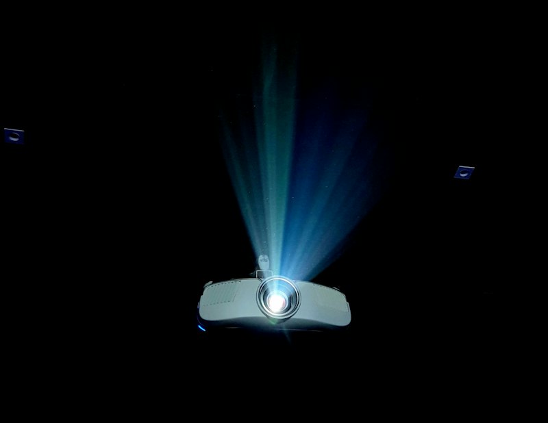 A compact white portable projector casting light in a darkened room