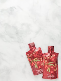 Two red pouches with the label 'NingXia Red' featuring images of goji berries and leaves are placed on a light marbled surface. The pouches are branded with 'Young Living' and contain essential oil-infused wolfberry supplement.