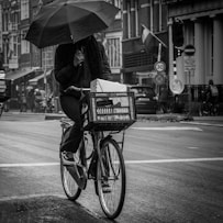 grayscale photography of person riding bicycle while holding umbrella