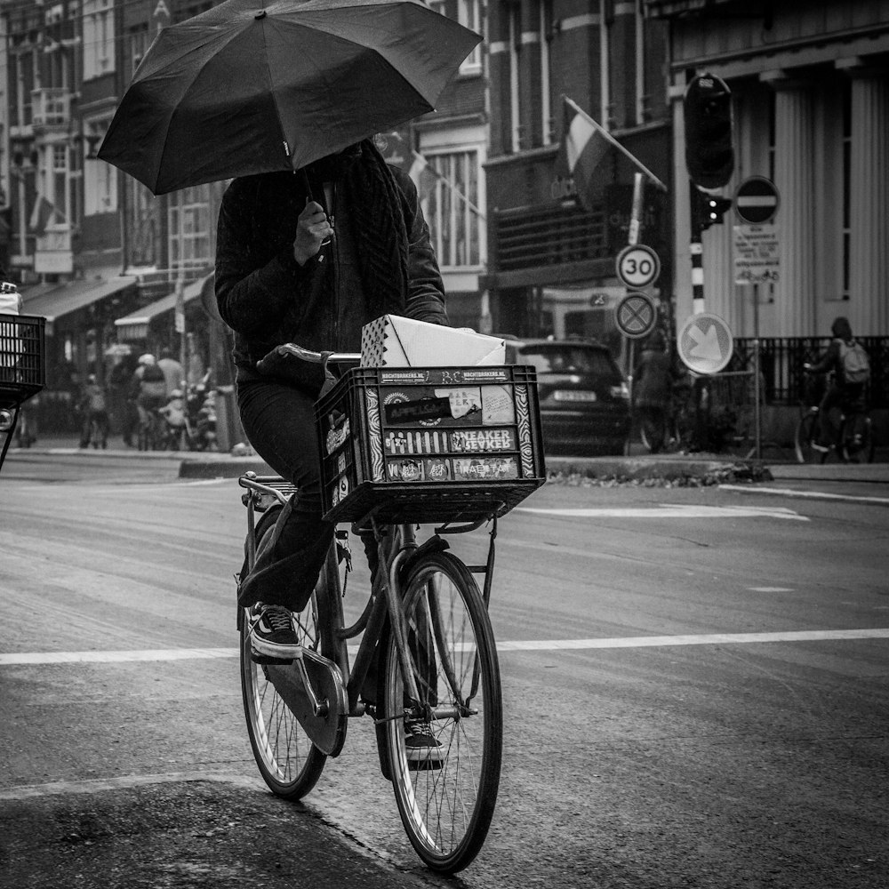 grayscale photography of person riding bicycle while holding umbrella