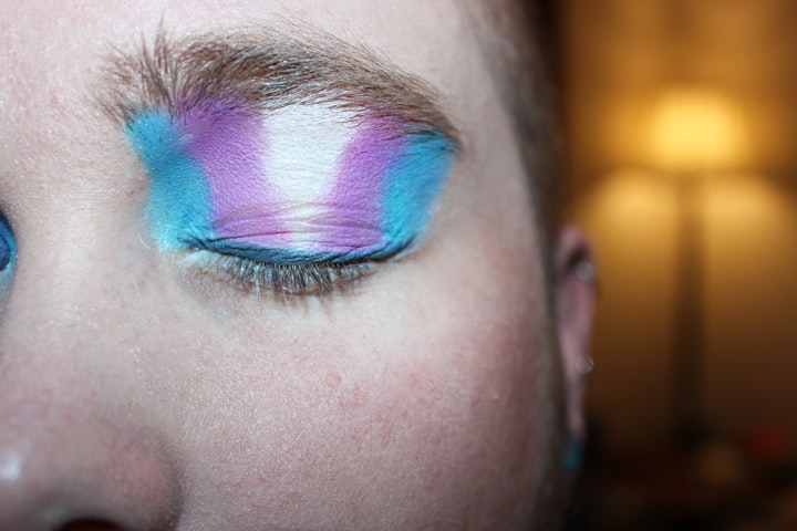 Closeup of a white persn's closed eye with eyeshadow in the colors of the trans flag. 