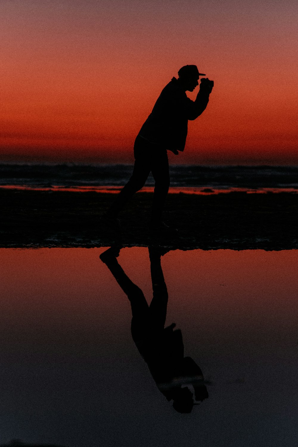 silhouette view of man taking photo at the beach during sunset