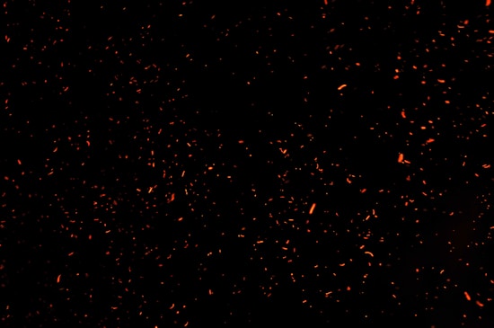 Numerous small, glowing orange sparks scattered across a dark background, creating a dynamic sense of movement and energy.
