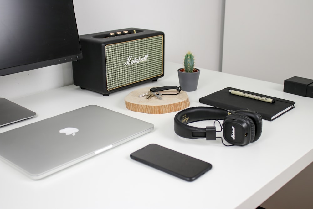 MacBook beside iPhone and headphones on white desk