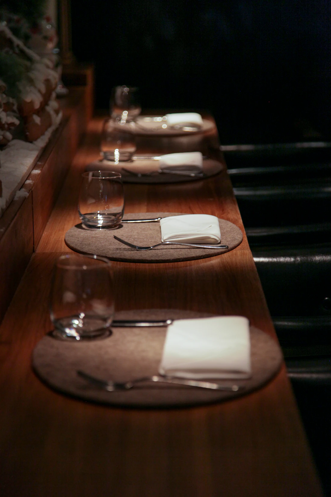 Row of place settings with napkins and glasses along a warm-lit wooden bar