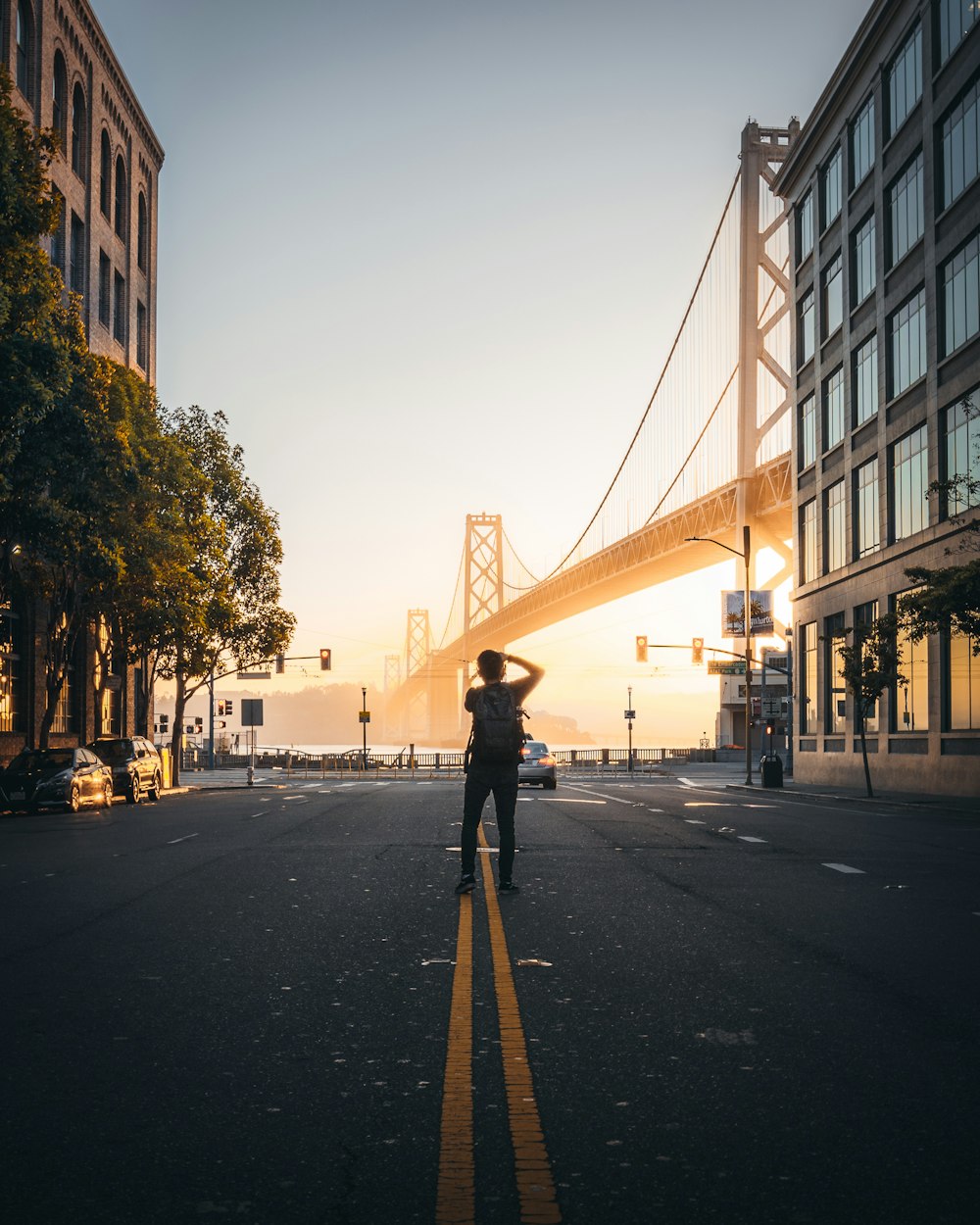 man takes photo of suspension bridge at the city during daytime