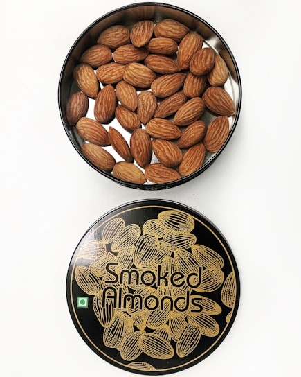 A container filled with almonds placed next to its lid. The lid has a stylish design with illustrations of almonds and the text 'Smoked Almonds' printed on it.