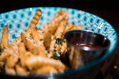 Golden crispy fries sprinkled with herbs served in a red container with a side of spicy sauce.
