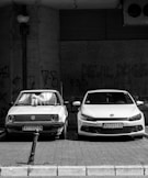 grayscale photo of two Volkswagen cars parked on sidewalk