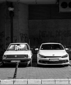 grayscale photo of two Volkswagen cars parked on sidewalk