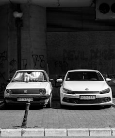 grayscale photo of two Volkswagen cars parked on sidewalk