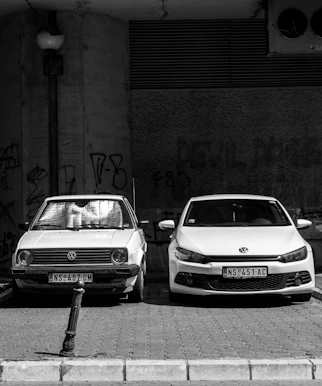 grayscale photo of two Volkswagen cars parked on sidewalk
